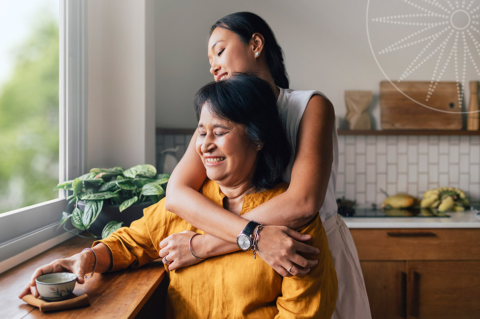 daughter hugging mom sitting down on a chair both looking out the window